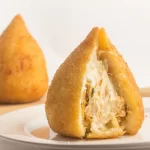 Coxinha de frango com catupiry aberta no prato.