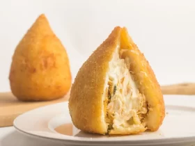 Coxinha de frango com catupiry aberta no prato.