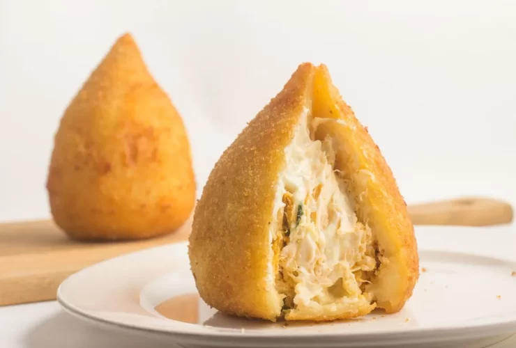 Coxinha de frango com catupiry aberta no prato.