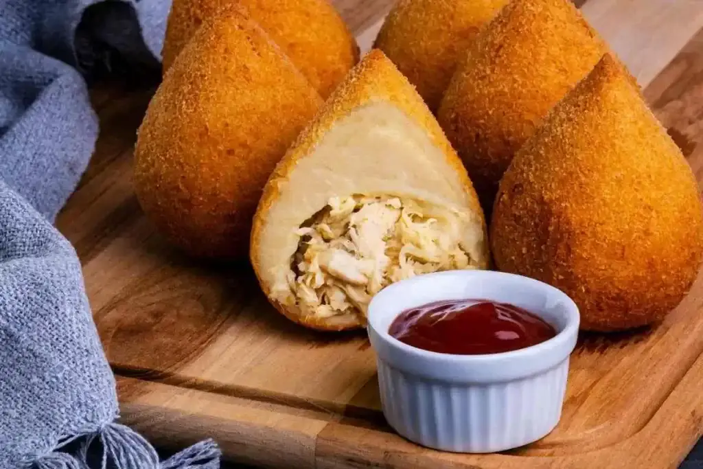 Coxinha de frango com recheio a mostra e um pouco de molho. 